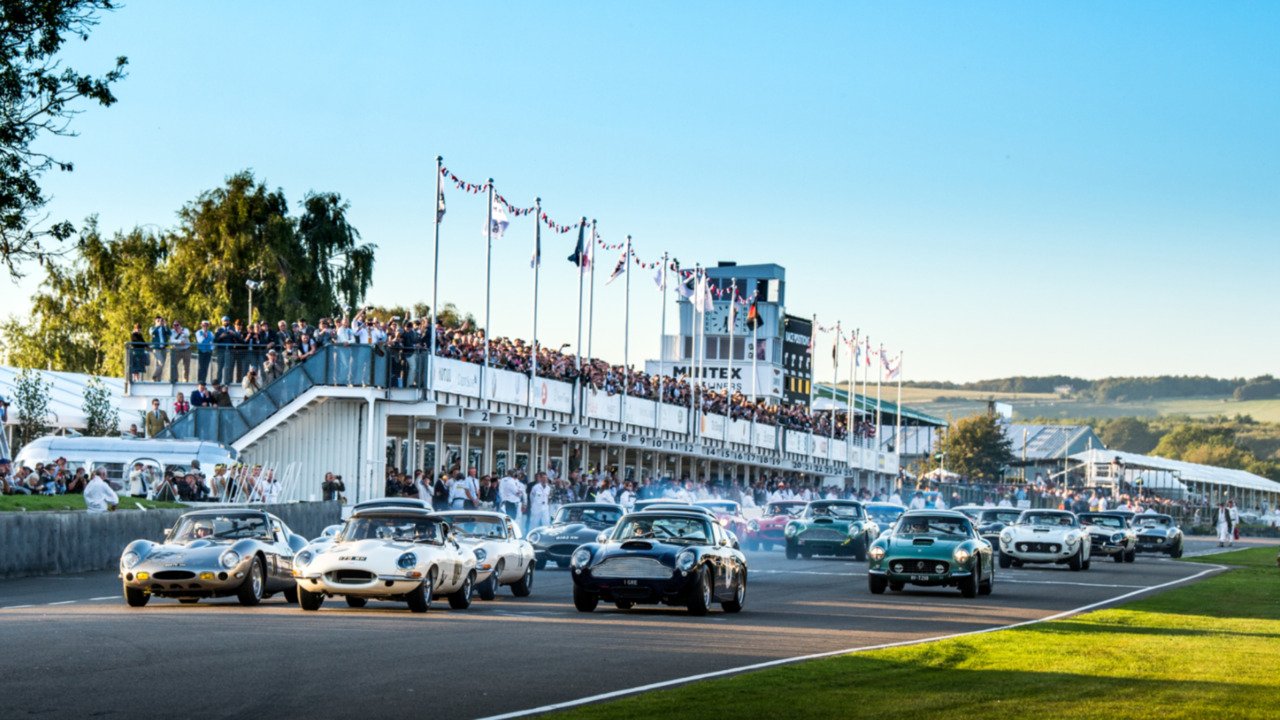 Classic car race at a historic motorsport event, with vintage sports cars speeding past a grandstand full of spectators waving flags